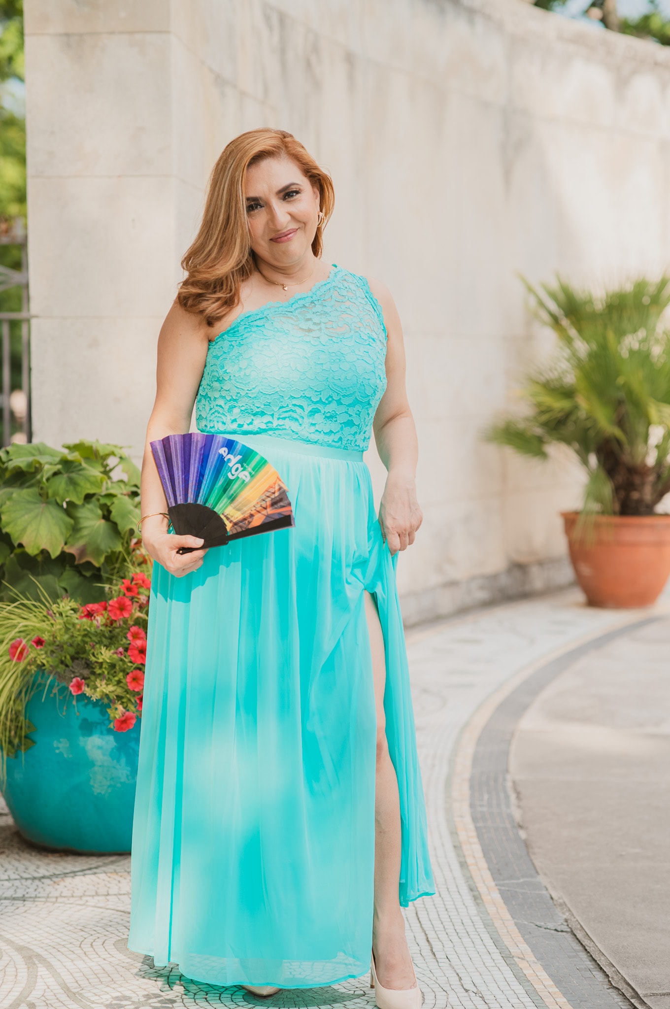 Outdoor portrait of a smiling woman in a long teal dress holding a colorful fan, by Fuentes Studio.