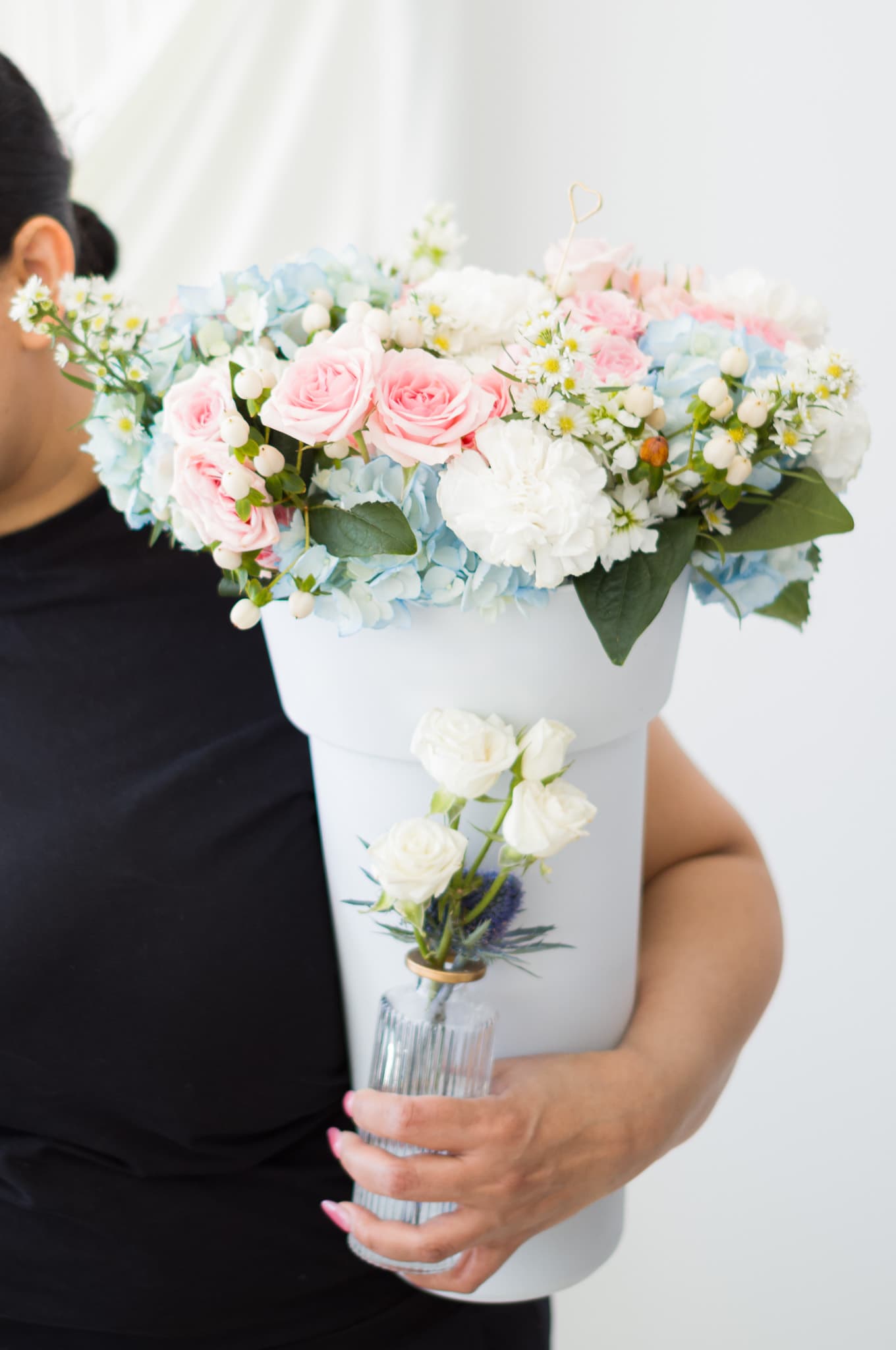A lush bouquet of pink roses, blue hydrangea, and white daisies wrapped in pink paper