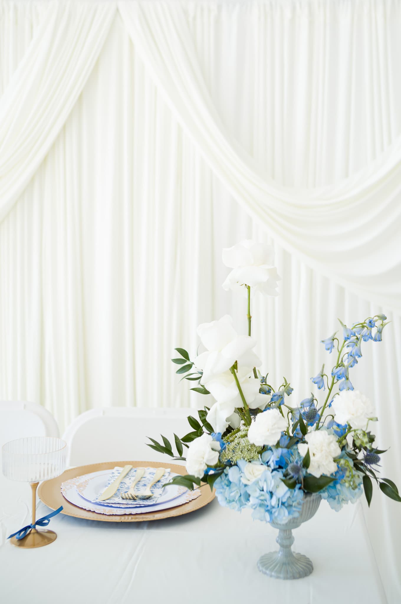 The full table setting with blue runner, gold chargers, floral centerpiece, and ribbed glassware
