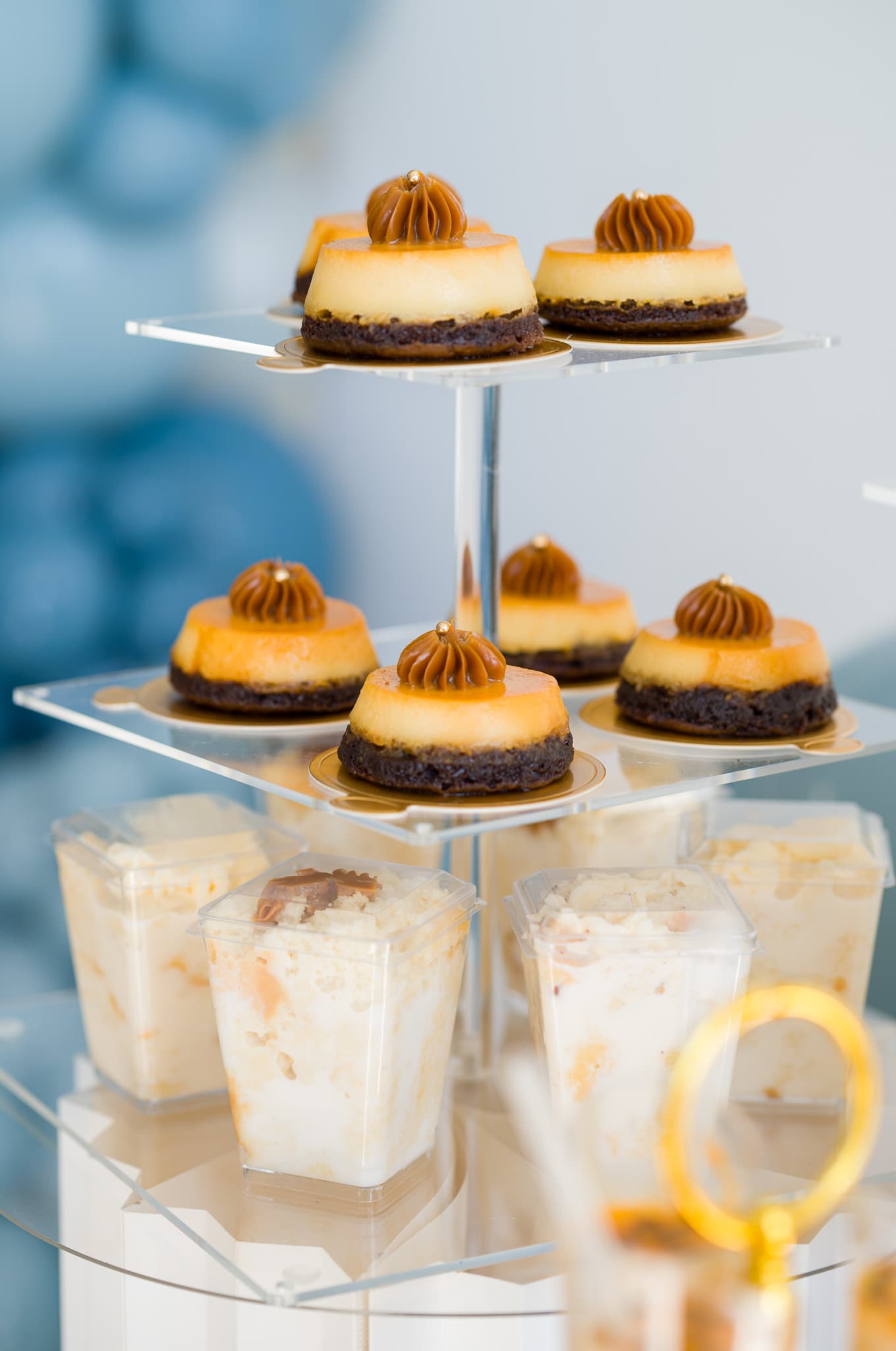 Tiered dessert display with caramel petit fours and cream parfaits against the blue balloon backdrop