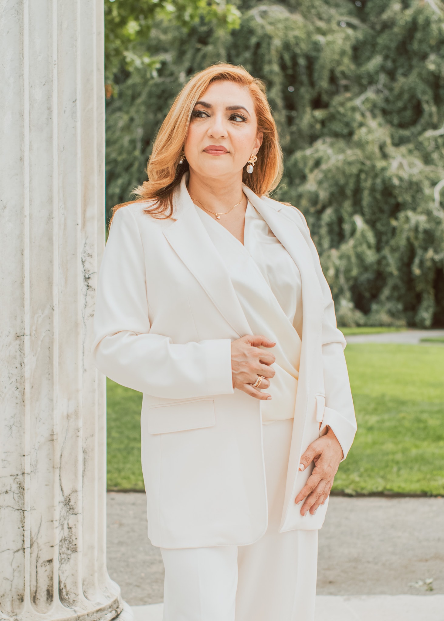 Professional portrait of a woman in an all-white pant suit standing next to a classical marble pillar outdoors Executive, Fuentes Studio NYC